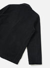 Flat lay detail shot of the black corduroy two-button jacket on a light grey seamless backdrop, showing the back and one sleeve. Fine wale corduroy texture is visible across the body and sleeve. Topstitched seams run along the armhole and hem. A small woven label patch sits at the lower back hem.
