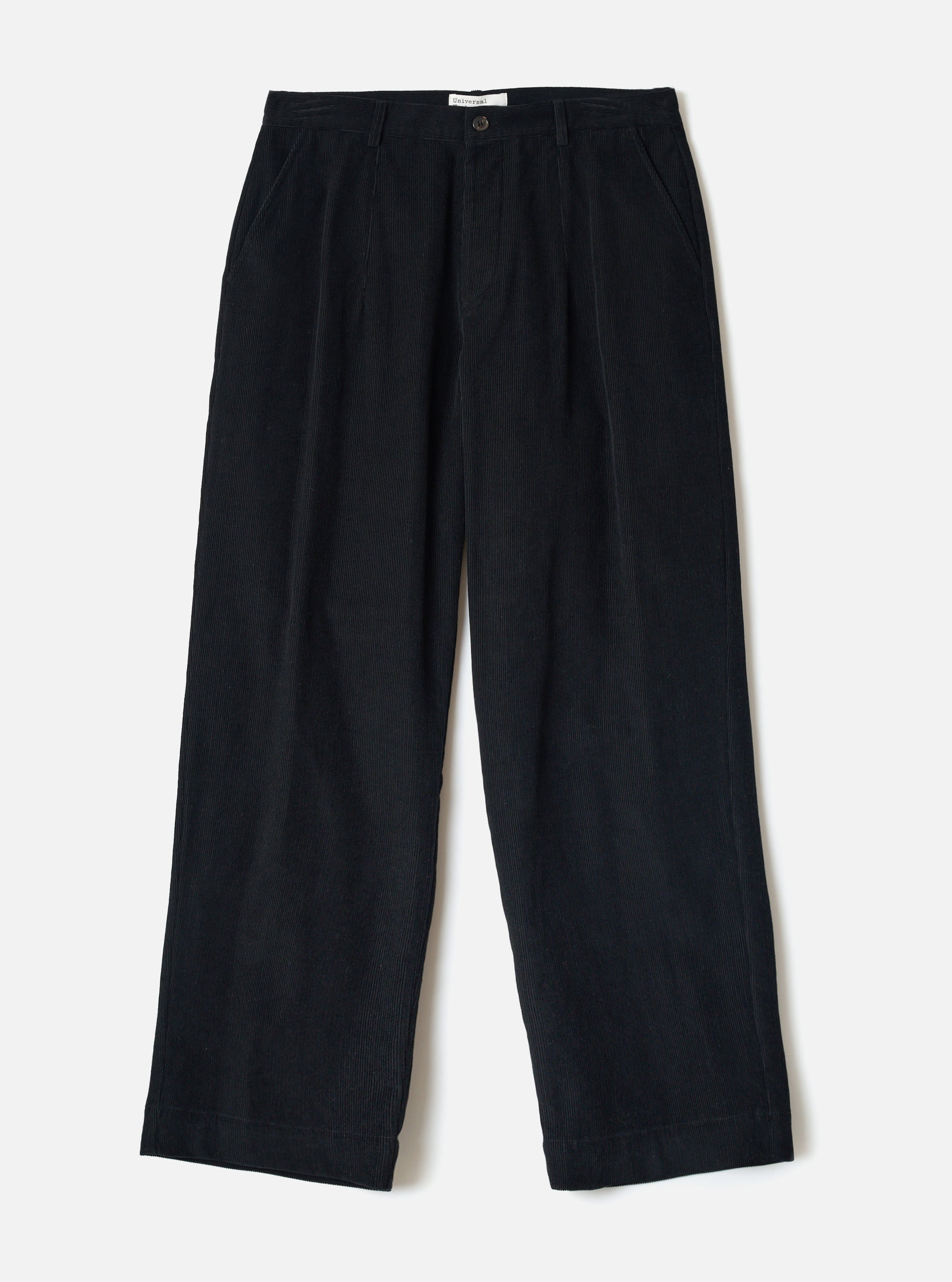Flat lay of black corduroy wide-leg chinos on a white studio backdrop. The ribbed cord texture is visible across the full length. Features a single button fly, front pleats, slant side pockets, belt loops, and a straight wide hem. A small branded label sits at the inner waistband.