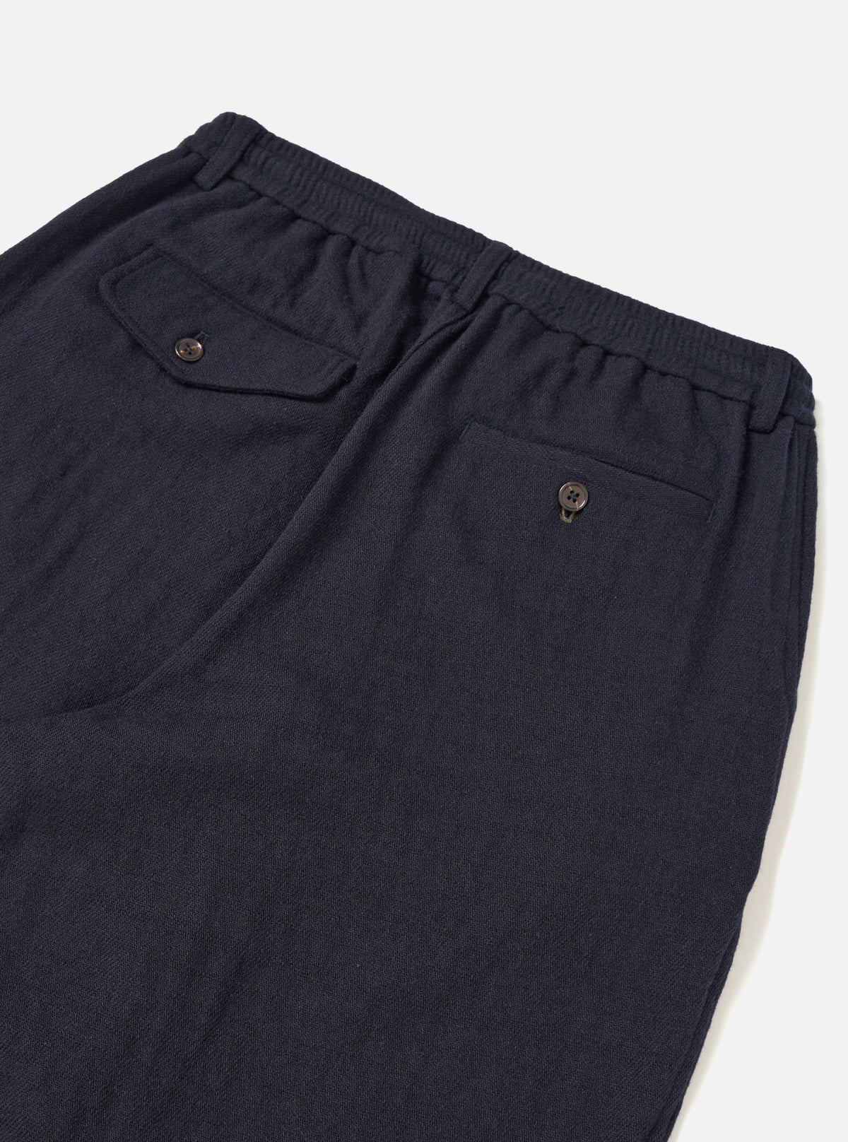 A male model wears the Dark Navy Robin Wool Mix Pleated Track Pant with a casual top, standing against a neutral studio backdrop. The full-length shot shows the tapered leg and loose fit.