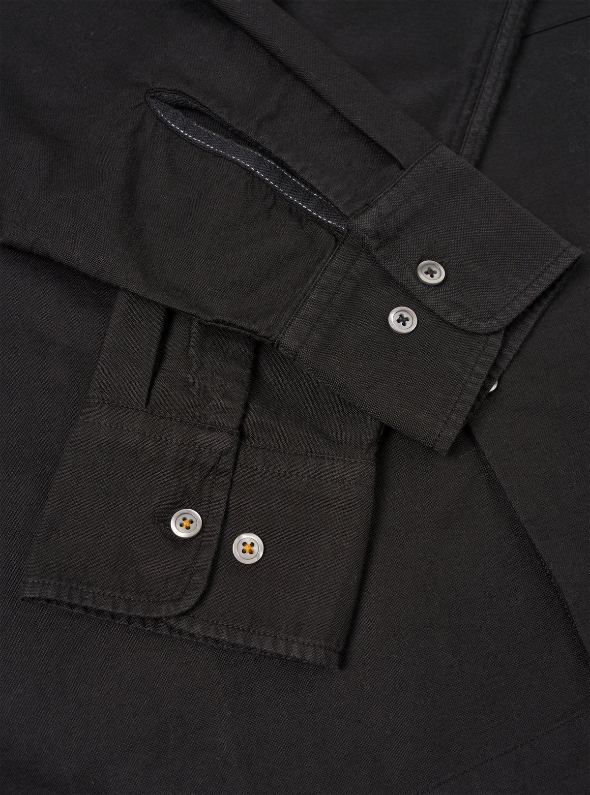 A male model wears the Black R.Oxford Lucky Shirt unbuttoned over a t-shirt against a neutral studio backdrop, demonstrating the loose fit and easy untucked style of the garment.