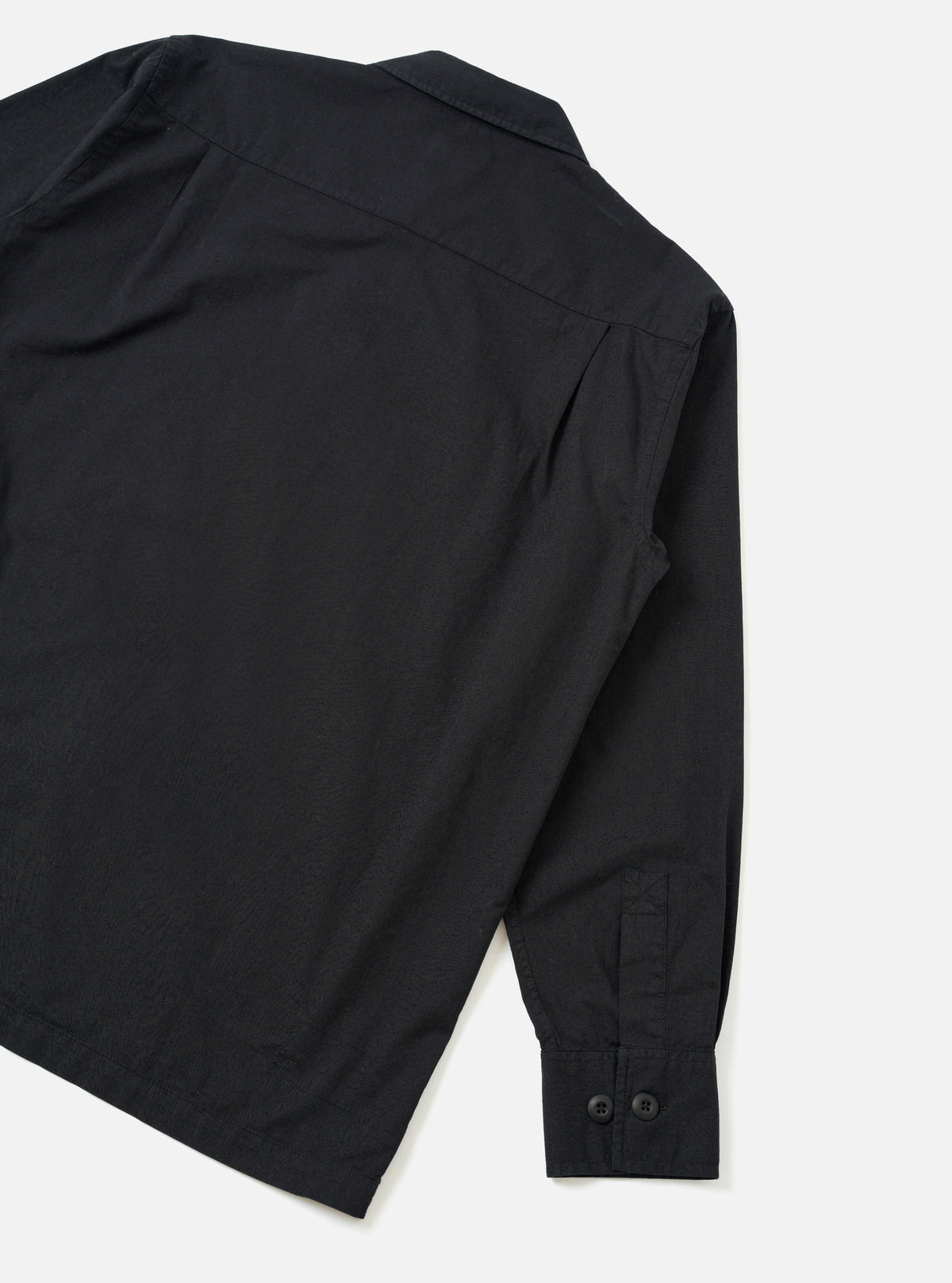 Rear view of the Black Slub Shirting Fatigue Shirt presented on a solid off-white background. The shot highlights the smooth back panel, clean hemline, straight shoulder seams, and slub texture of the cotton fabric.