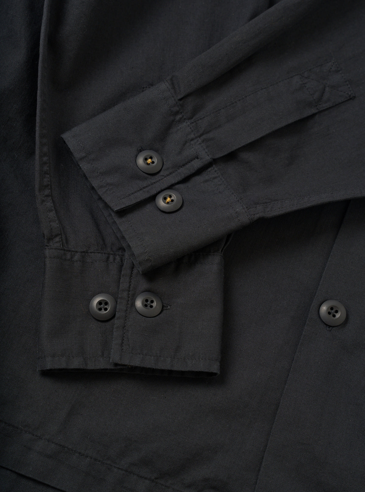 A detailed close-up shot of the Black Slub Shirting Fatigue Shirt set against a plain background. The view emphasizes the textured slub cotton fabric, neat chest pocket stitching, and front button closure details.