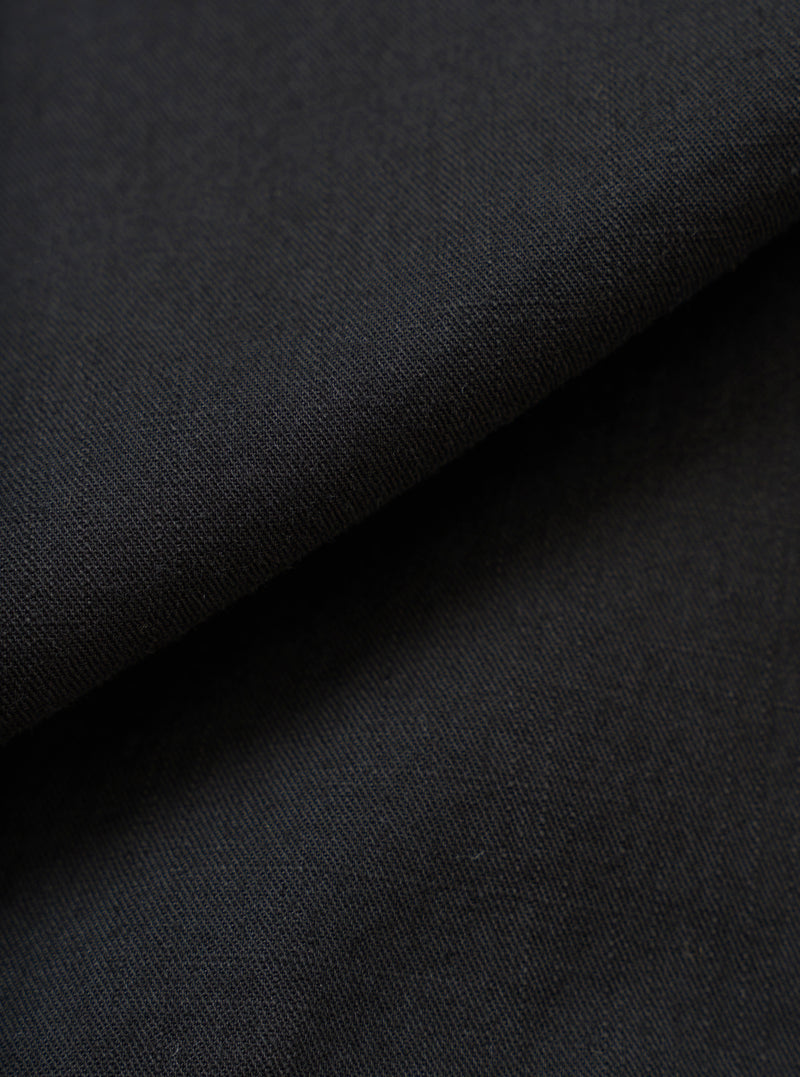 A full-frame fabric swatch image detailing the rich texture and weave of the Black Slub Shirting Fatigue Shirt. The macro shot highlights the subtle slub cotton pattern and dark tone of the material up close.