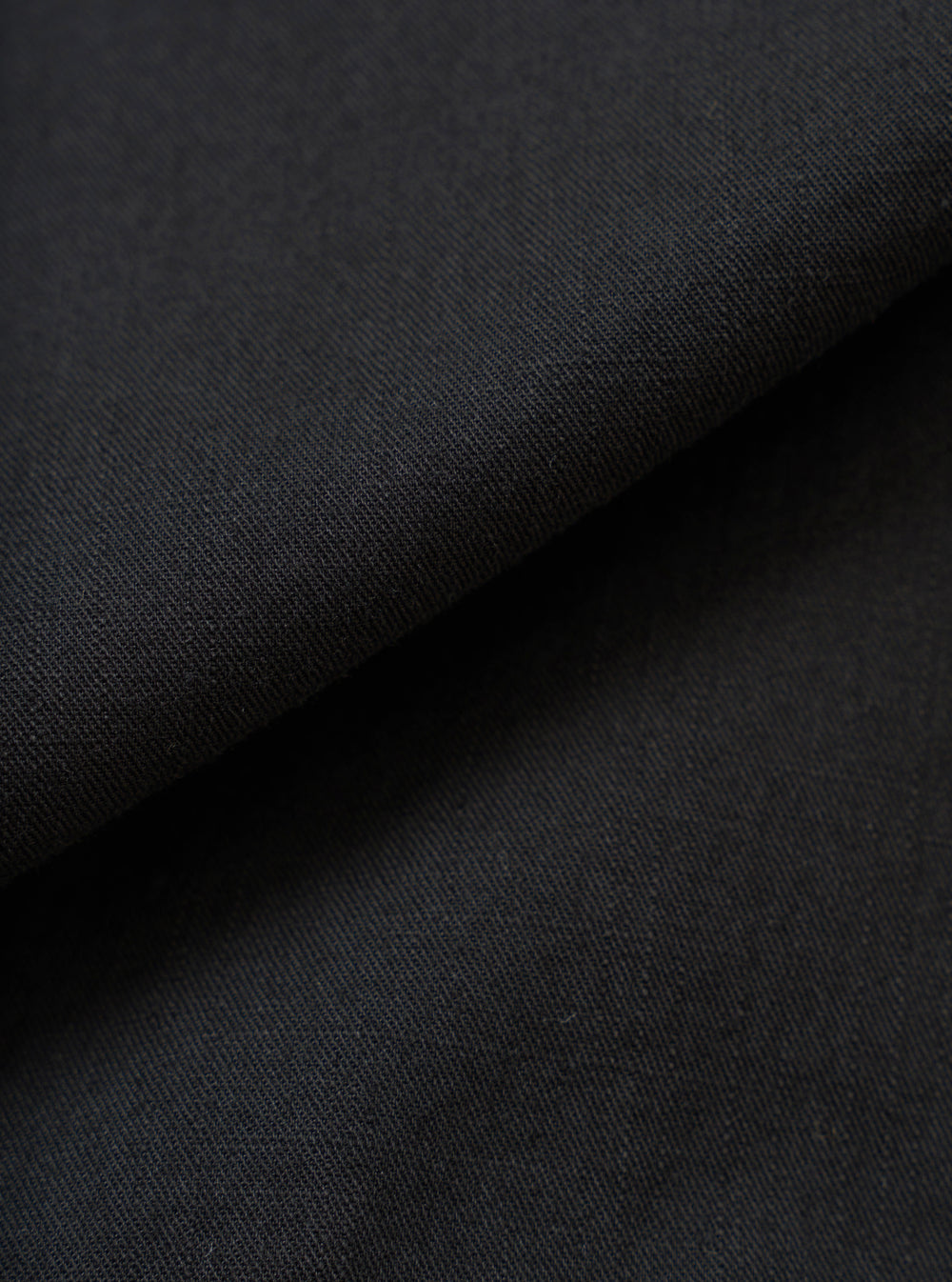 A full-frame fabric swatch image detailing the rich texture and weave of the Black Slub Shirting Fatigue Shirt. The macro shot highlights the subtle slub cotton pattern and dark tone of the material up close.
