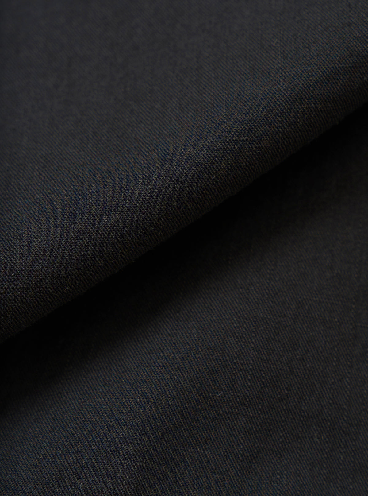 A full-frame fabric swatch image detailing the rich texture and weave of the Black Slub Shirting Fatigue Shirt. The macro shot highlights the subtle slub cotton pattern and dark tone of the material up close.