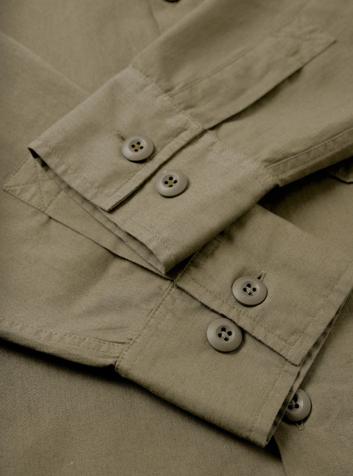 A close-up detail shot of the Olive Slub Shirting Fatigue Shirt against a plain background, highlighting the rich slub texture of the cotton fabric alongside fine stitching around the button closures and chest pocket.