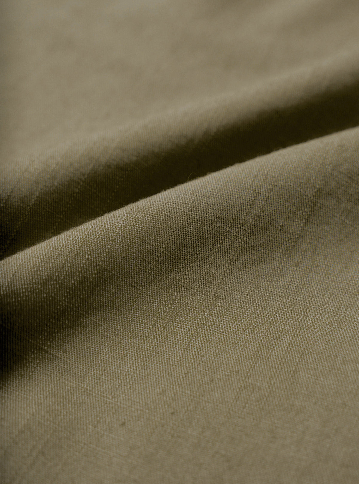 A macro fabric swatch image showing the fine weave and soft slub texture of the Olive Slub Shirting Fatigue Shirt. The close-up view fills the frame to display the distinct olive green shade and cotton material structure.