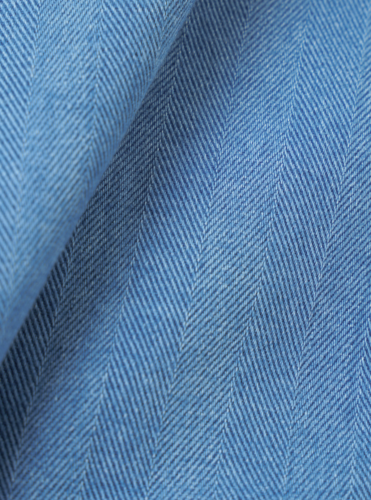 A macro fabric swatch view showing the intricate weave and soft texture of the Washed Indigo Recycled Herringbone Patch Lucky Shirt. The close-up fills the frame to display the indigo shade and fabric pattern.
