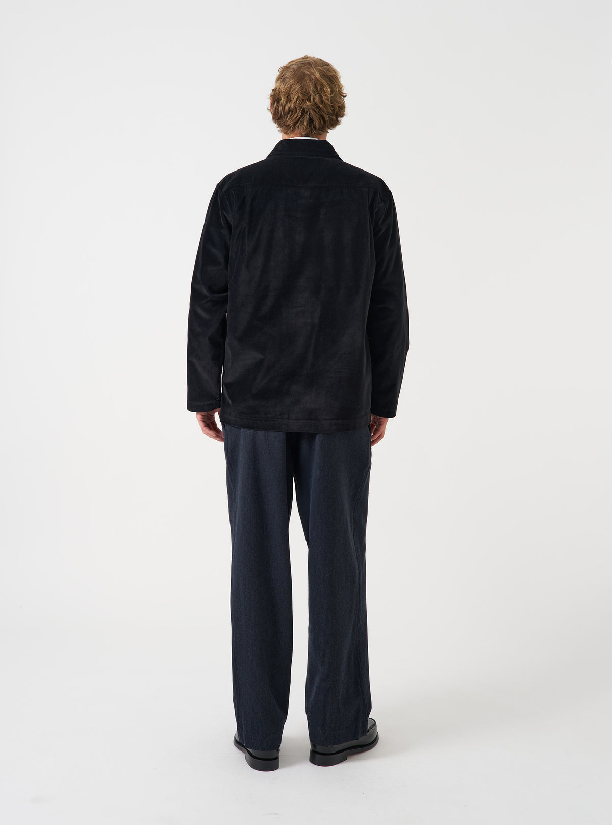 A male model wears the Black CPH Velvet Dockside jacket unbuttoned over a light top, captured in a full-length pose against a neutral studio background. The shot displays the garment's relaxed fit and casual styling.