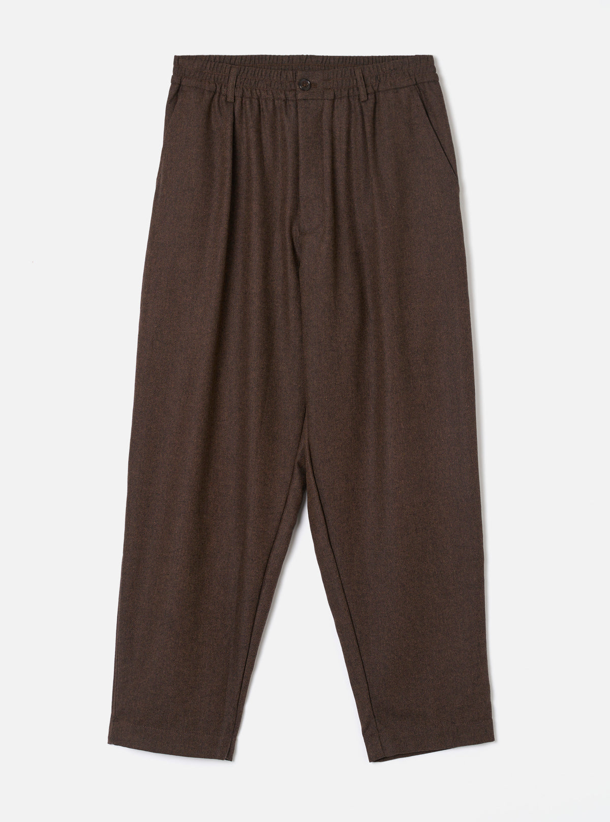 A full-length front view of a model wearing the Brown Recycled Italian Tweed Pleated Track Pant in a studio setting. The image showcases the relaxed tapered fit, drawstring waist, and warm brown tweed fabric.