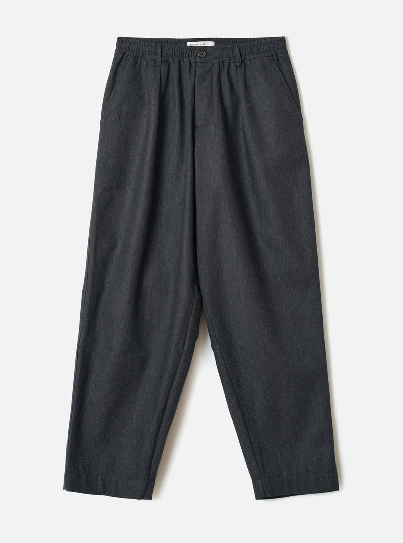 A full-length front view of a model wearing the Charcoal Recycled Italian Tweed Pleated Track Pant in a studio backdrop. The shot showcases the tapered fit, front pleats, and dark grey tweed fabric.