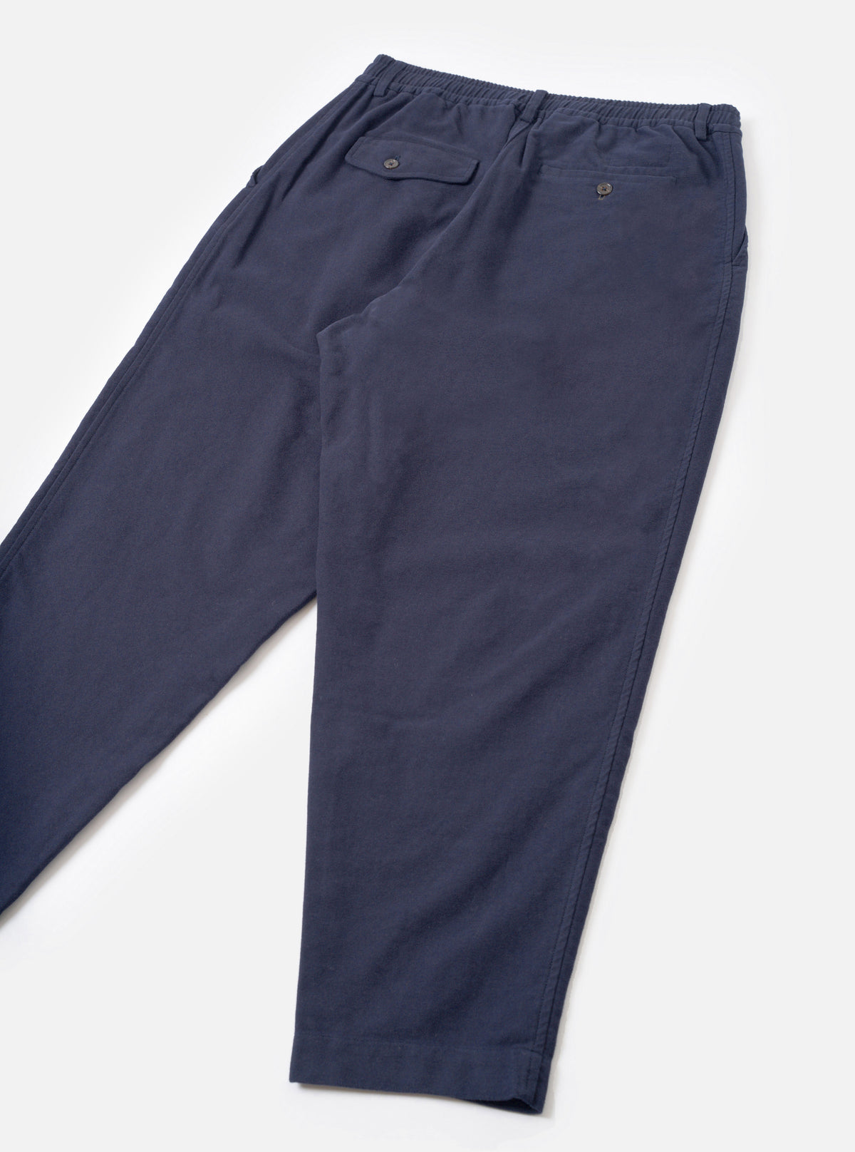 A back view product image of the Navy Comfort Moleskin Pleated Track Pant against a plain white background, highlighting the rear buttoned flap pocket, clean stitching, and dark navy brushed cotton moleskin fabric.