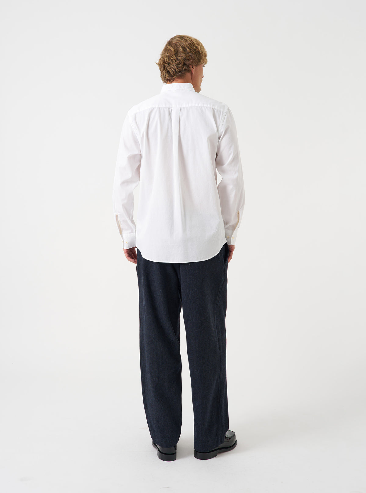 A rear angle photograph of a model wearing the Navy Airline Flannel Oxford Pant in a neutral studio environment, demonstrating the wide silhouette, tailored drape, and back pocket detailing.