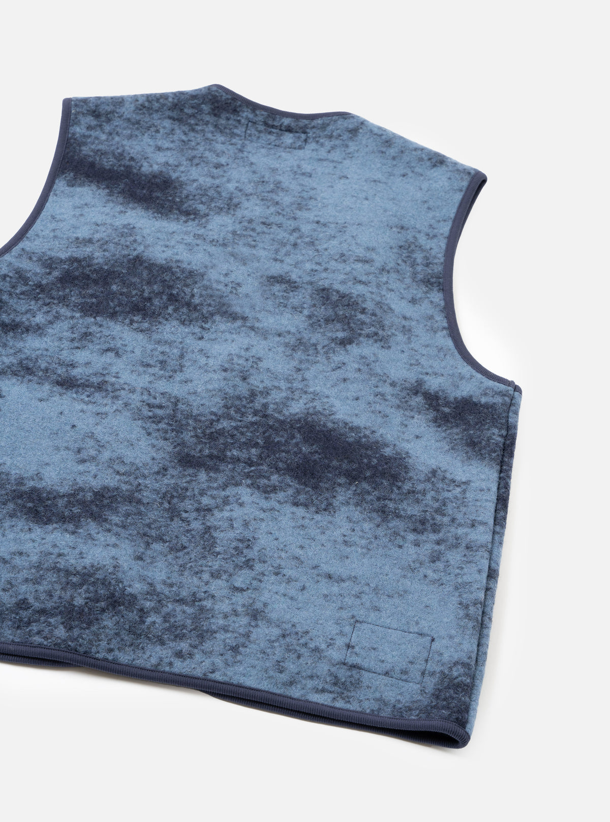 A back view of a model wearing the Blue Cloud Camo Knit Zip Gilet against a plain background, showing the back cut, armhole finishing, ribbed hem, and striking blue cloud camouflage wool knit pattern.