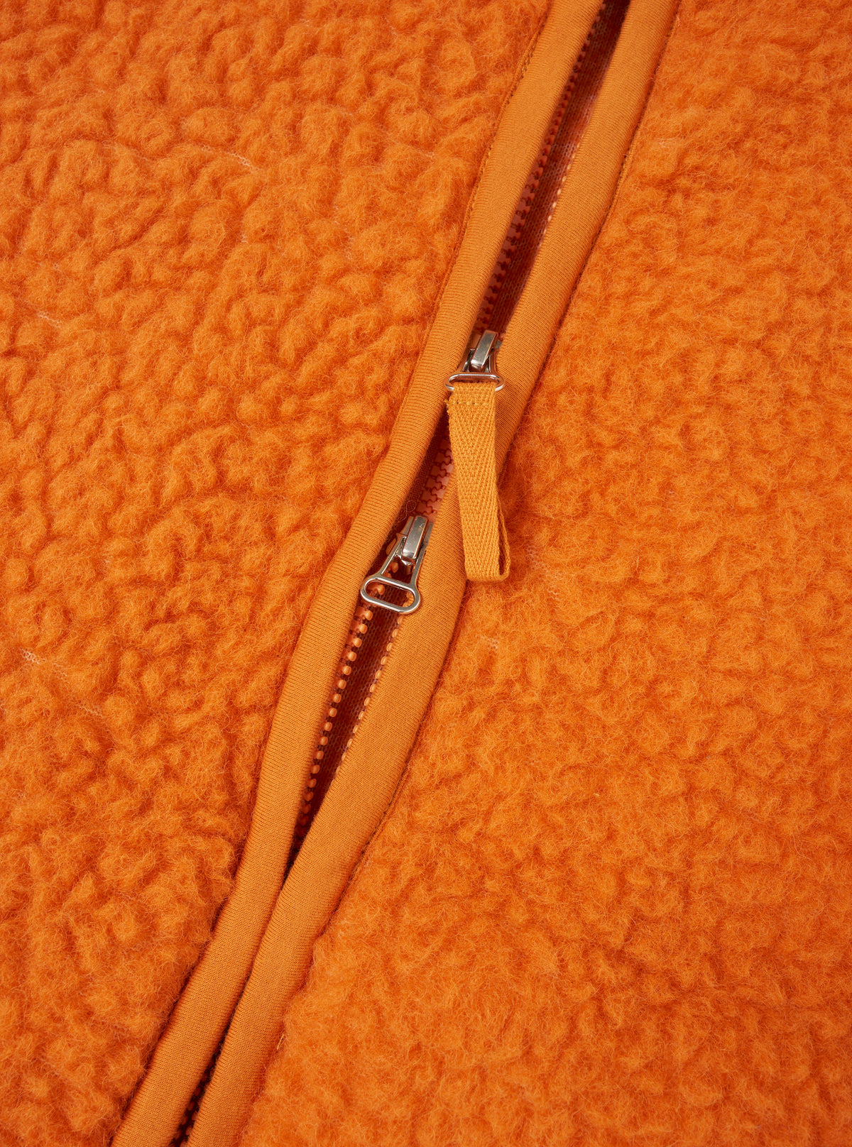 Close-up detail shot of the Orange Artic Fleece Hep Mountain Jacket on a plain background, focusing on the zip hardware, chest pocket seam, and rich orange fleece fabric texture.