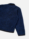 Close-up rear view of the blue boucle style fleece Lancaster jacket on a plain light grey studio backdrop. The textured boucle style fabric shows a navy and cobalt mottled finish. A dark navy collar, cuff trim, and hem band are visible, contrasting with the main body. One sleeve is shown in full.
