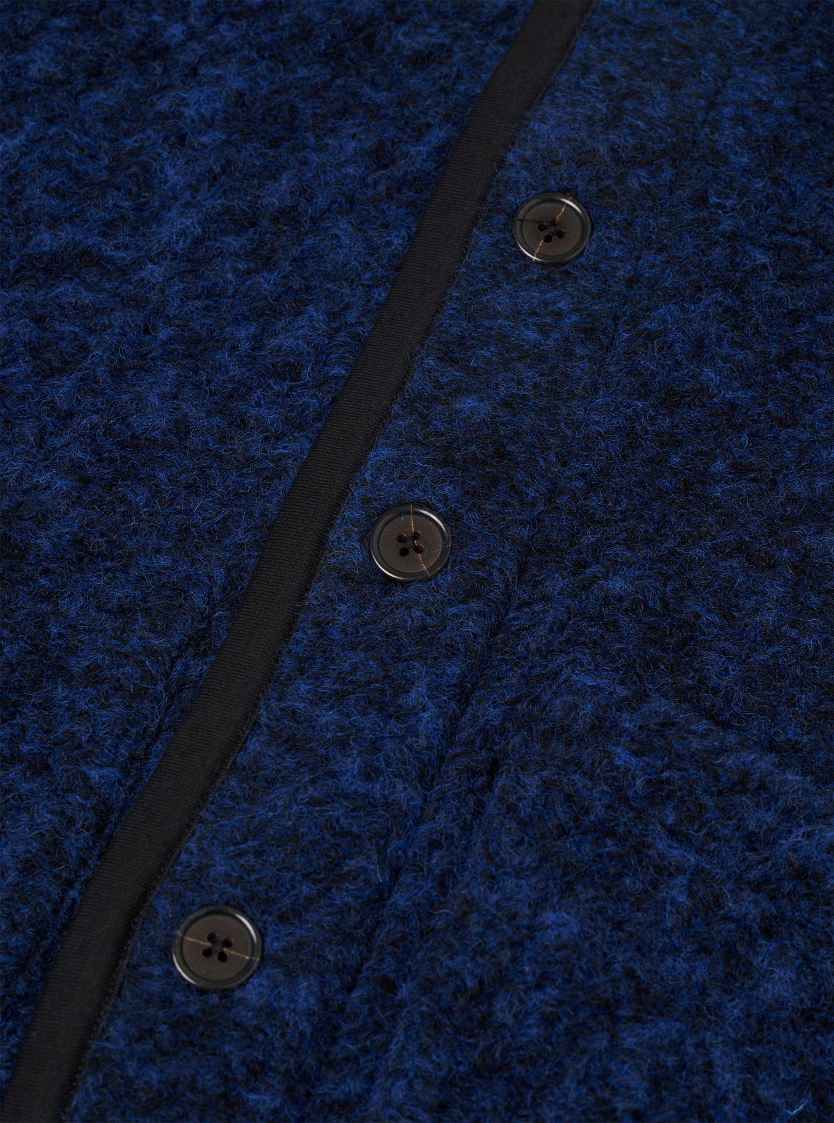 Close-up detail of the blue boucle style fleece Lancaster jacket, showing three dark four-hole buttons fastened along a narrow black grosgrain placket trim. The boucle style texture is prominent, with a dense, looped navy and blue marl surface. Shot against a plain white studio backdrop.