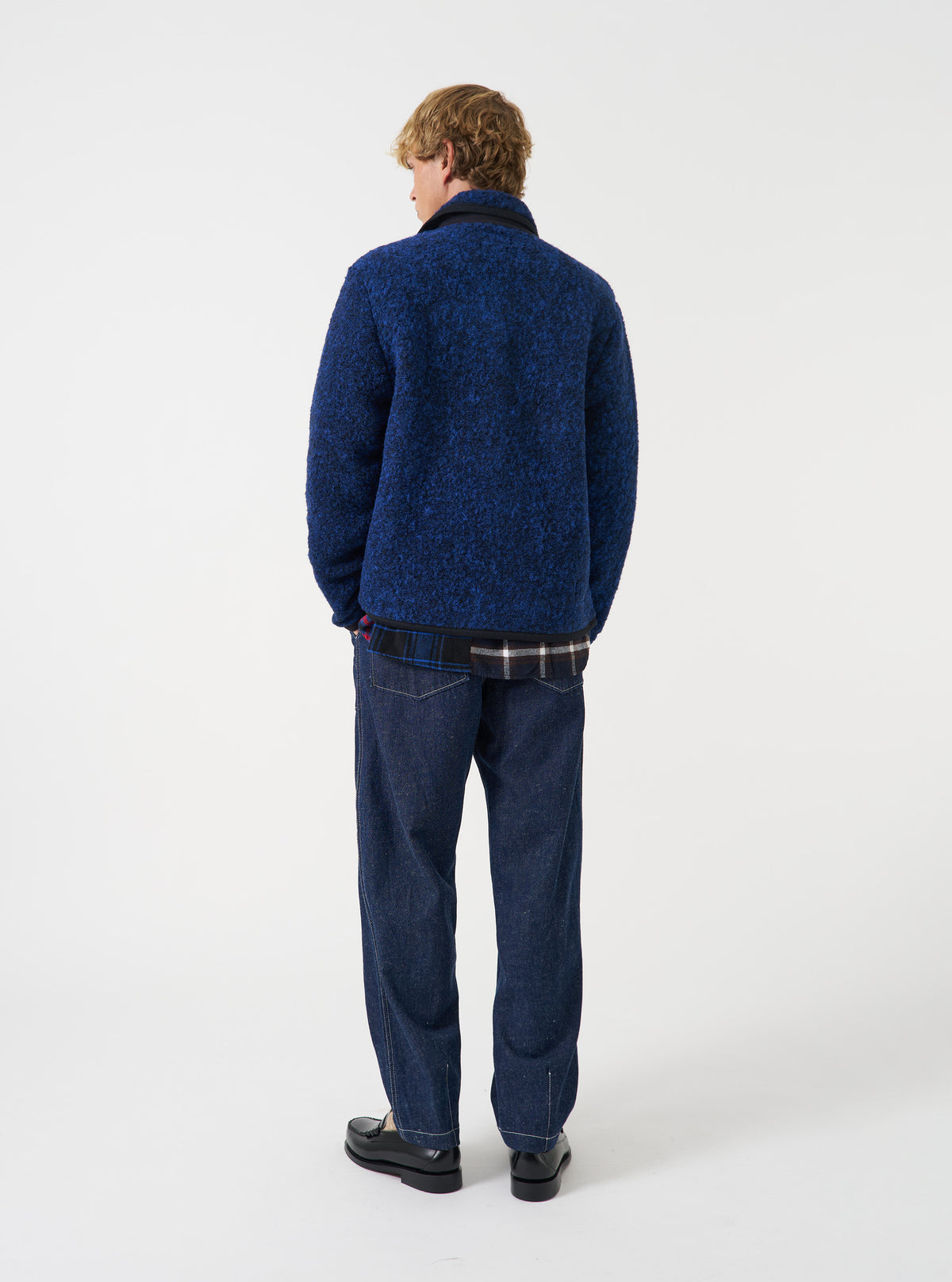 Back view of a model wearing the Blue Bouclet Fleece Lancaster Jacket in a studio setting. The photograph showcases the clean fit across the shoulders, straight hemline, and textured bouclé fleece material in deep blue.