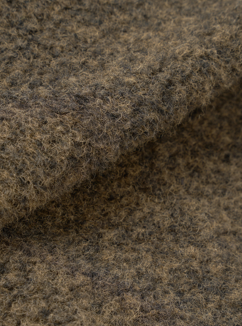 Close-up of the brown boucle style fleece fabric used in the Lancaster Jacket. The texture shows dense, tightly looped fibres with a mix of dark brown and tan tones, creating a coarse, woolly surface. The fabric is folded to reveal its thick, plush depth against a neutral studio background.