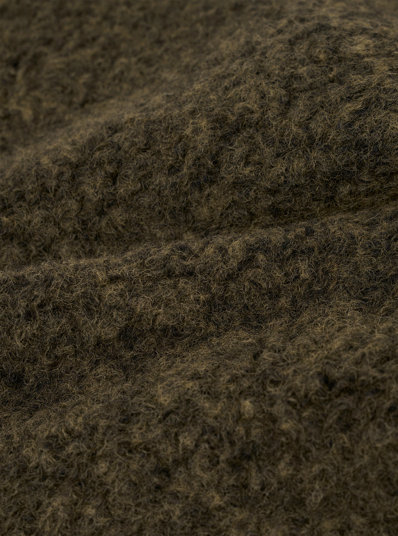 Close-up of the brown boucle style fleece fabric used in the Lancaster Jacket. The texture shows dense, tightly looped fibres with a mix of dark brown and tan tones, creating a coarse, woolly surface. The fabric is folded to reveal its thick, plush depth against a neutral studio background.