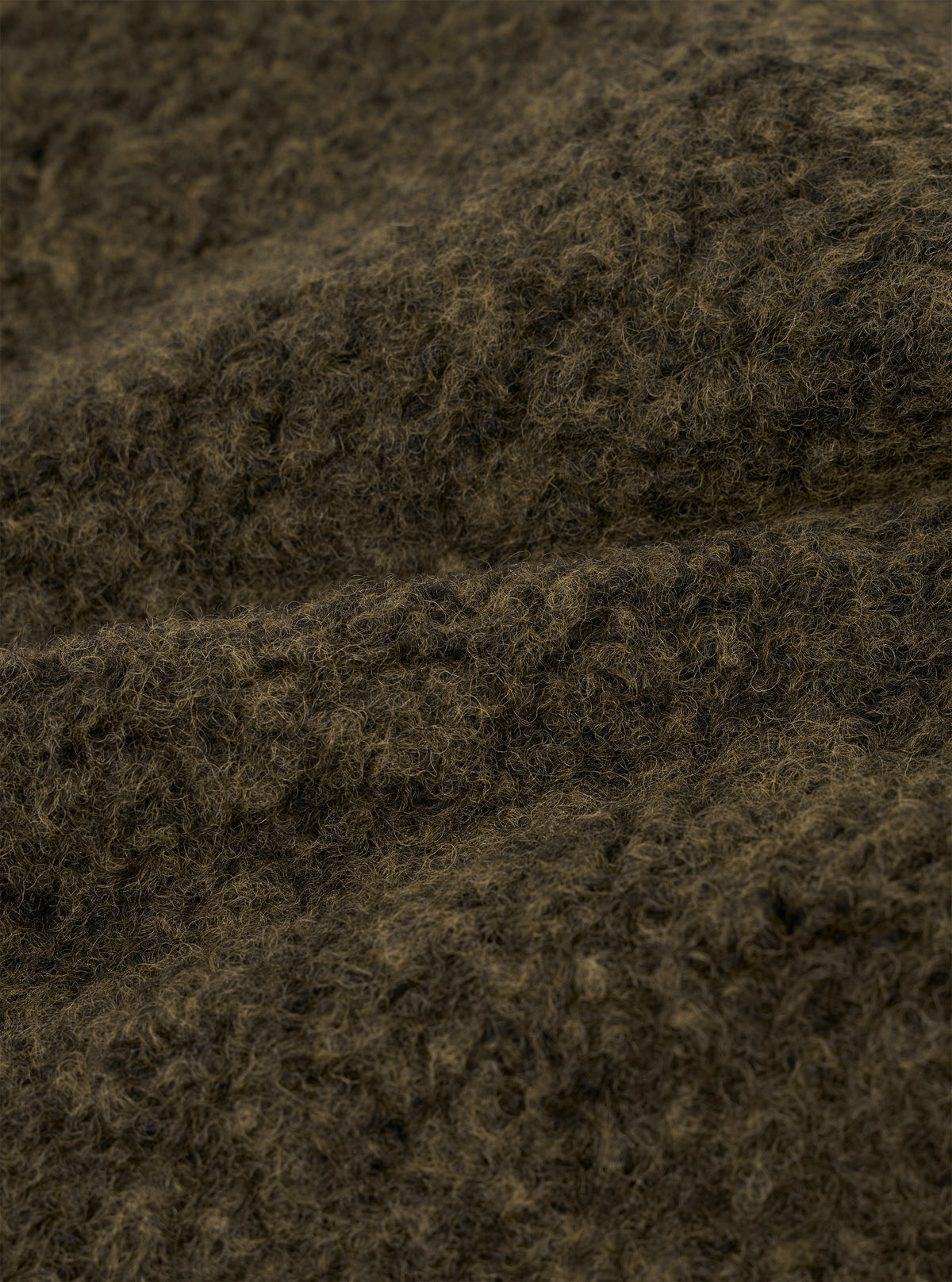 Close-up of the brown boucle style fleece fabric used in the Lancaster Jacket. The texture shows dense, tightly looped fibres with a mix of dark brown and tan tones, creating a coarse, woolly surface. The fabric is folded to reveal its thick, plush depth against a neutral studio background.