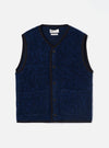 Blue boucle style fleece gilet laid flat on a light grey studio backdrop. V-neckline with dark navy binding trim running around the neck, armholes, front placket and hem. Five dark horn-effect buttons down the centre front. Two patch pockets at the lower front. Textured blue and black marl boucle style fabric throughout. Universal Works label visible at the neckline.
