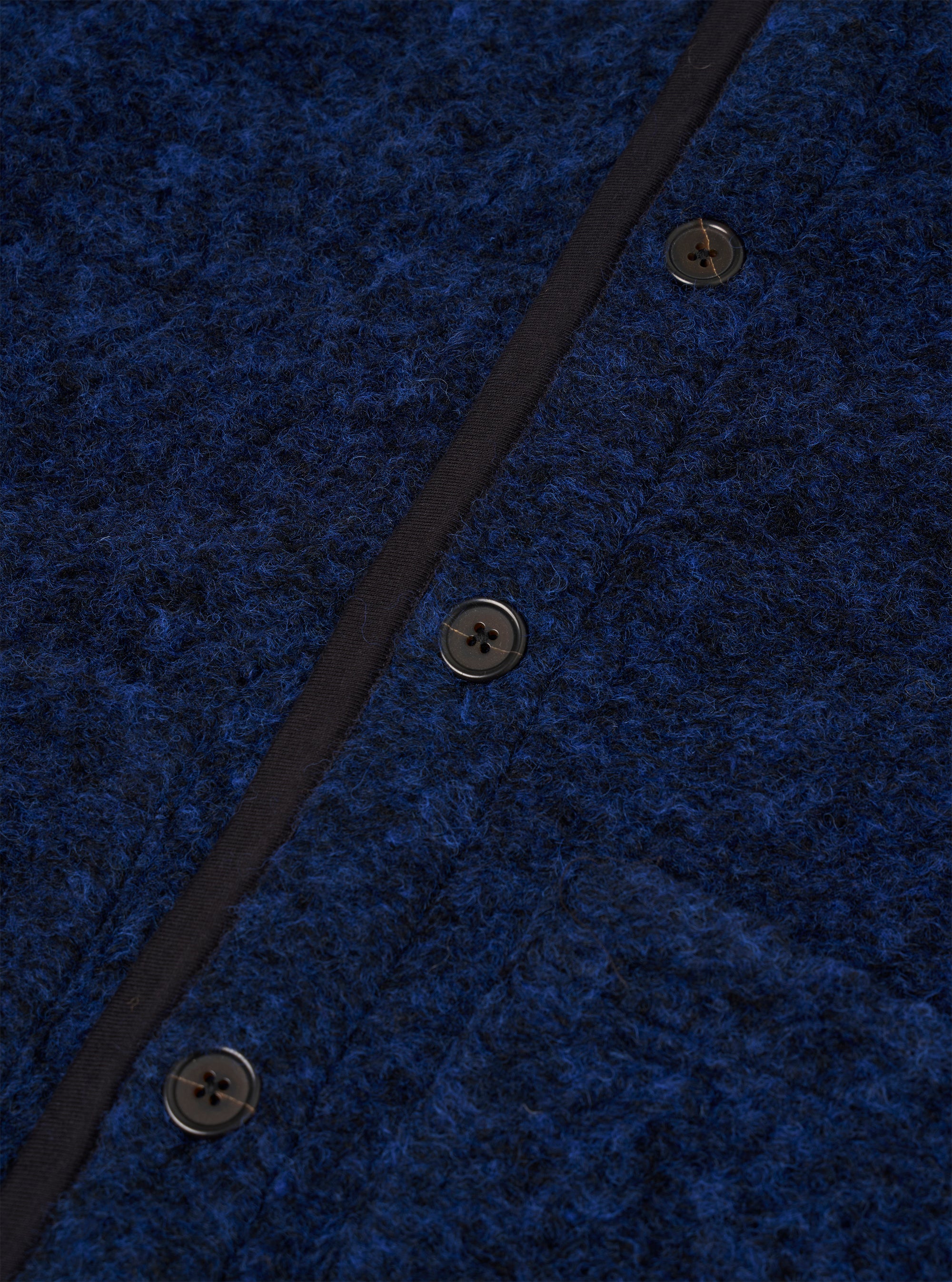 Close-up of the blue boucle style fleece Lancaster gilet, showing three dark four-hole buttons fastened along a navy grosgrain placket. The textured boucle style fabric has a looped, flecked surface in cobalt and dark navy tones. No model or mannequin is present.
