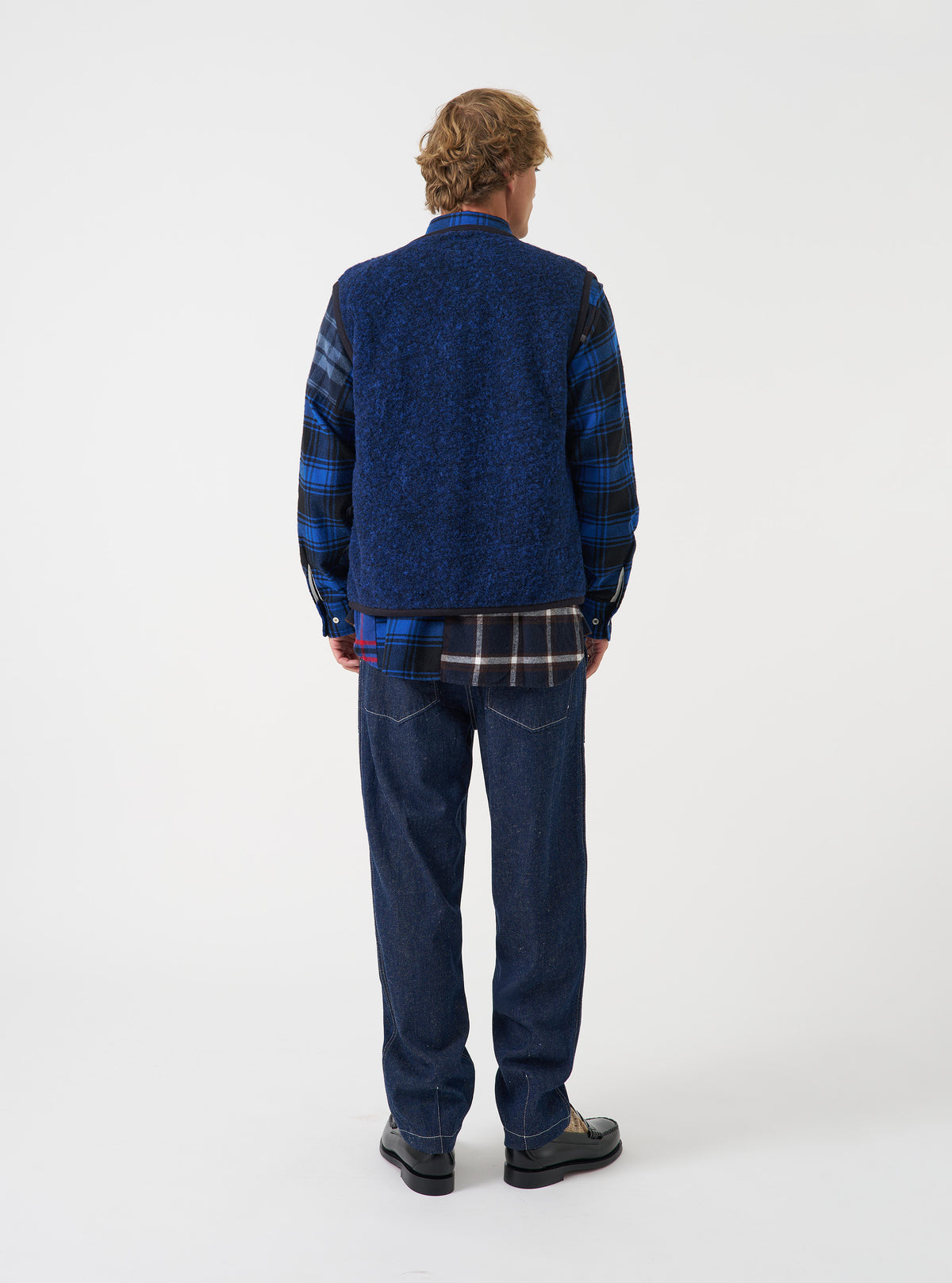Rear view of a model wearing the Blue Bouclet Fleece Lancaster Gilet against a plain studio background. The shot emphasizes the clean back construction, armhole cuts, and soft blue bouclé fleece texture.