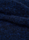Close-up detail shot of the navy blue boucle style fleece fabric used in the Lancaster Gilet. The texture shows a tightly looped, fluffy boucle style weave with flecks of bright blue running through a darker navy base, giving a soft, voluminous surface. Fabric is folded to show depth and loft.