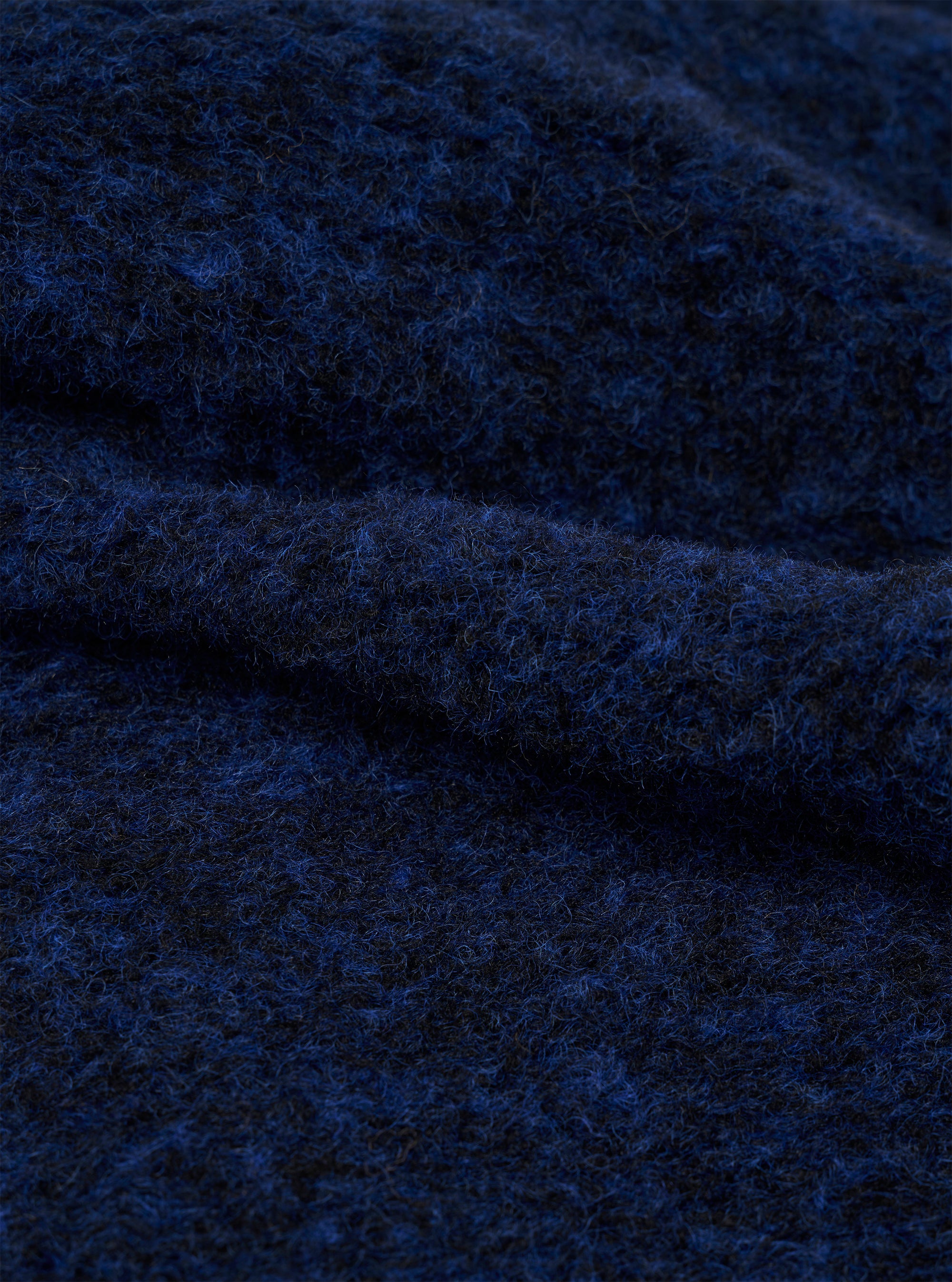 Close-up detail shot of the navy blue boucle style fleece fabric used in the Lancaster Gilet. The texture shows a tightly looped, fluffy boucle style weave with flecks of bright blue running through a darker navy base, giving a soft, voluminous surface. Fabric is folded to show depth and loft.