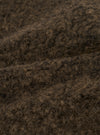 Close-up detail shot of the brown boucle style fleece fabric used in the Lancaster Gilet. The tightly looped, curly texture is clearly visible, with dark brown and warm tan tones running through the fibres. The image shows the fabric folded, highlighting its depth and soft, fluffy surface.