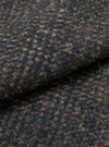 Close-up of the fabric of a navy sleeveless crew knit, showing a textured weave with flecks of camel and blue throughout. The fabric is folded, highlighting its soft, looped surface and medium weight. No background visible.