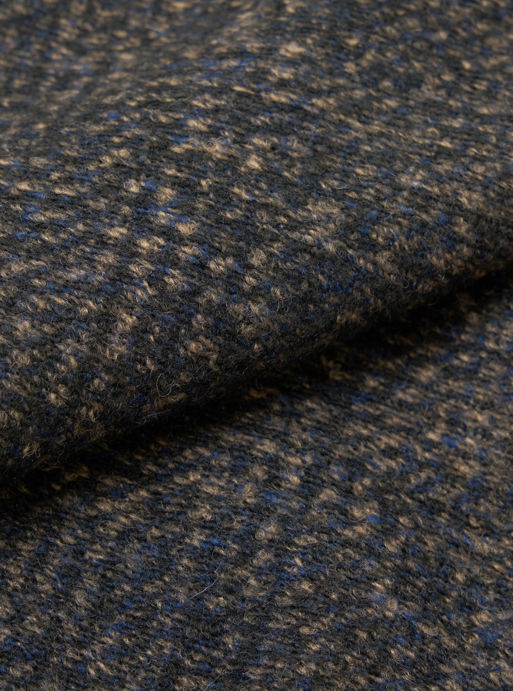 Close-up of the fabric of a navy sleeveless crew knit, showing a textured weave with flecks of camel and blue throughout. The fabric is folded, highlighting its soft, looped surface and medium weight. No background visible.