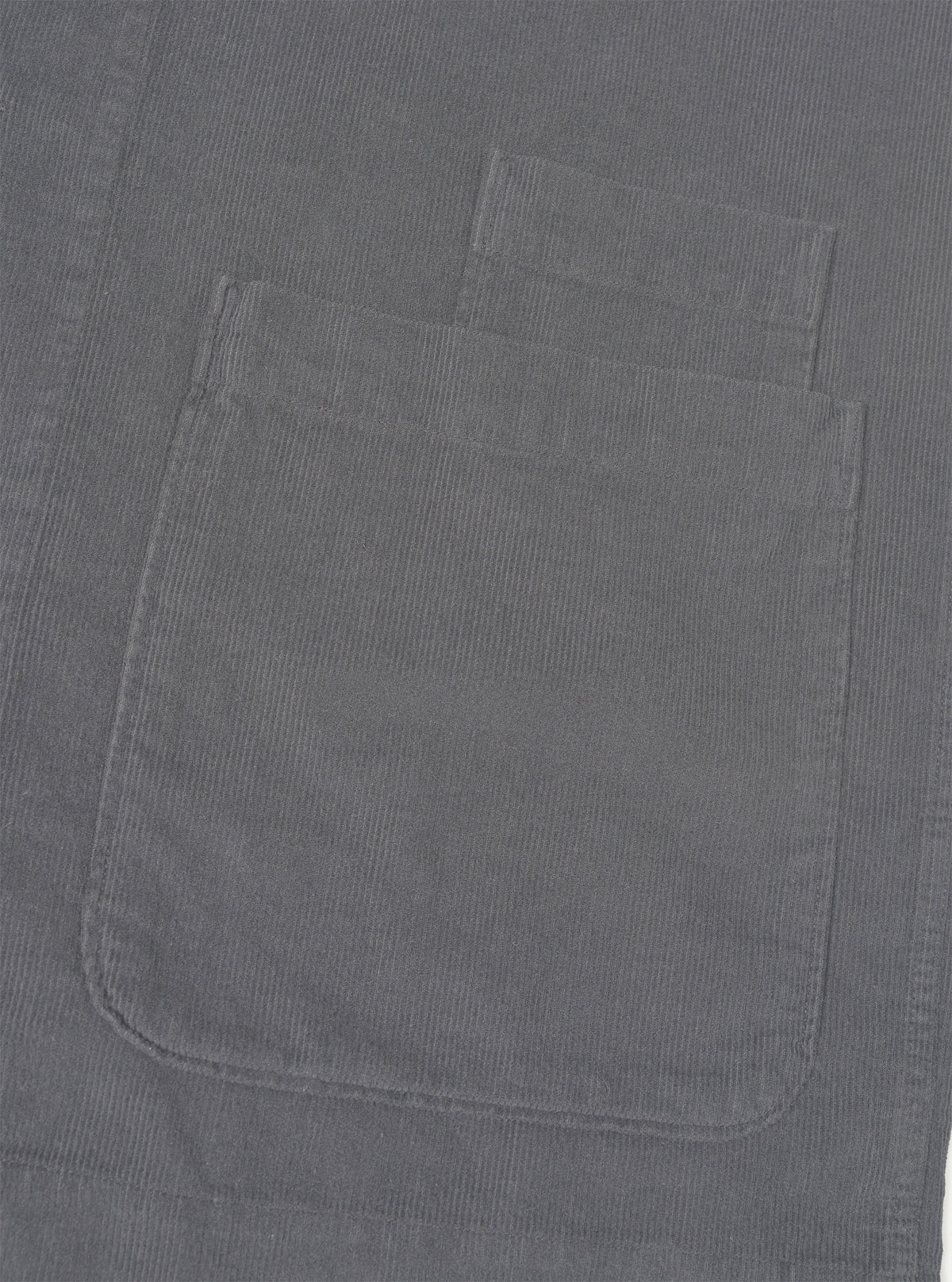 A close-up shot of the Universal Works Grey Fine Cord Bakers Overshirt on a white background, highlighting the fine corduroy fabric texture, collar, chest pocket, and front button details.