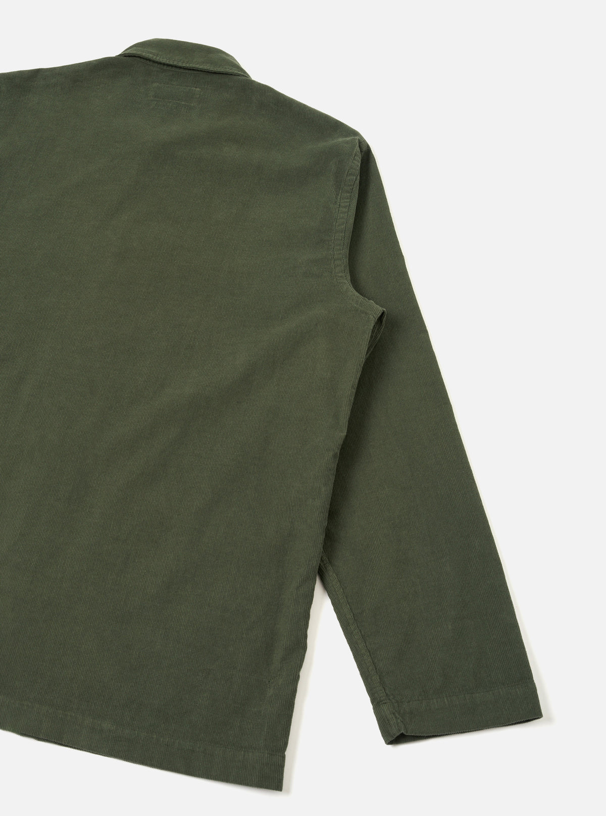 Back view of a male model wearing the Universal Works Olive Fine Cord Bakers Overshirt, displaying the relaxed fit, straight hem, and fine-wale olive green corduroy fabric against a plain white background.
