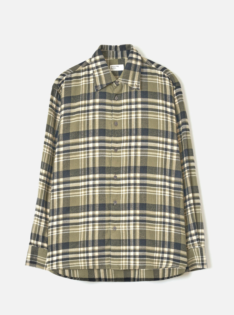 A male model wearing the Universal Works Olive Jazz Check Standard Shirt, standing against a plain off-white background, displaying the classic button-down style, olive checked pattern, and crisp collar.