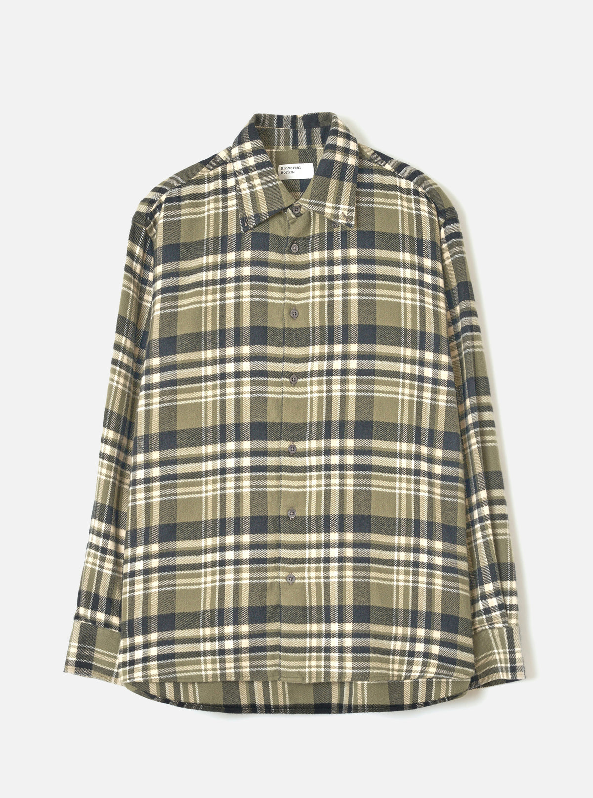 A male model wearing the Universal Works Olive Jazz Check Standard Shirt, standing against a plain off-white background, displaying the classic button-down style, olive checked pattern, and crisp collar.