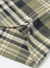 A side profile view of a male model wearing the Universal Works Olive Jazz Check Standard Shirt against a plain backdrop, featuring the buttoned cuffs, clean sleeve line, and subtle checked pattern.