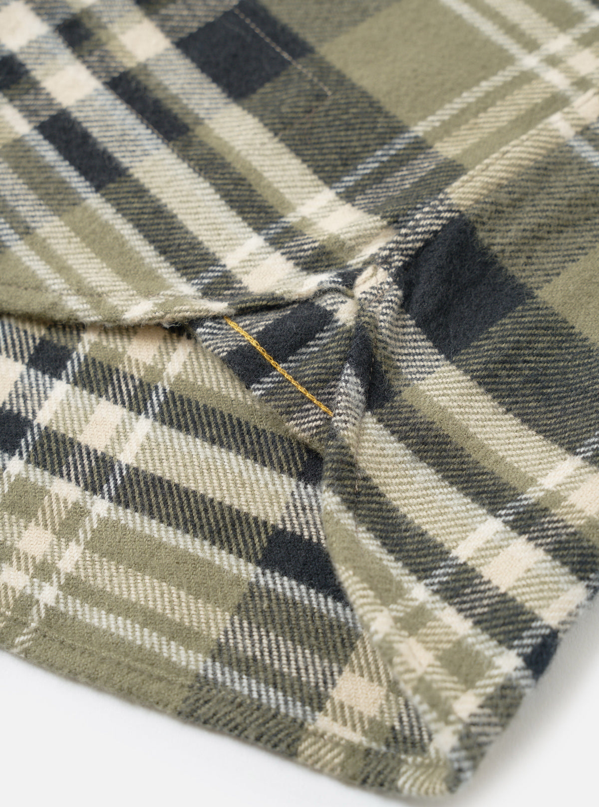 A side profile view of a male model wearing the Universal Works Olive Jazz Check Standard Shirt against a plain backdrop, featuring the buttoned cuffs, clean sleeve line, and subtle checked pattern.