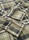 A close-up shot of the Universal Works Olive Jazz Check Standard Shirt, showing the neat collar, front button placket, and detailed olive woven jazz check pattern against a plain background.
