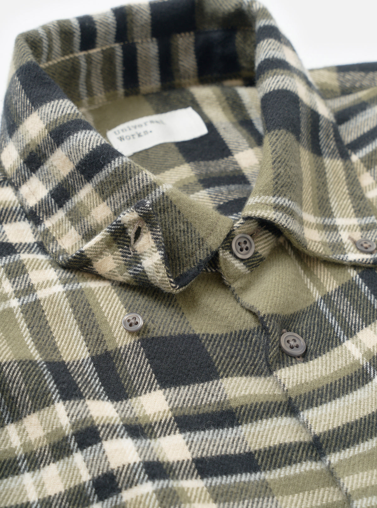 A detailed close-up shot focusing on the cuff and sleeve construction of the Universal Works Olive Jazz Check Standard Shirt, highlighting the organic cotton weave and tonal buttoning detail.