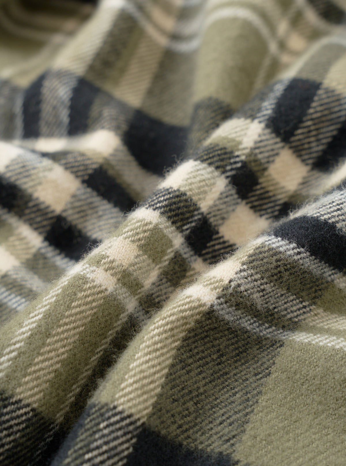 An extreme close-up fabric swatch of the Universal Works Olive Jazz Check Standard Shirt, showcasing the intricate organic cotton jazz check pattern and olive green weave in rich detail.