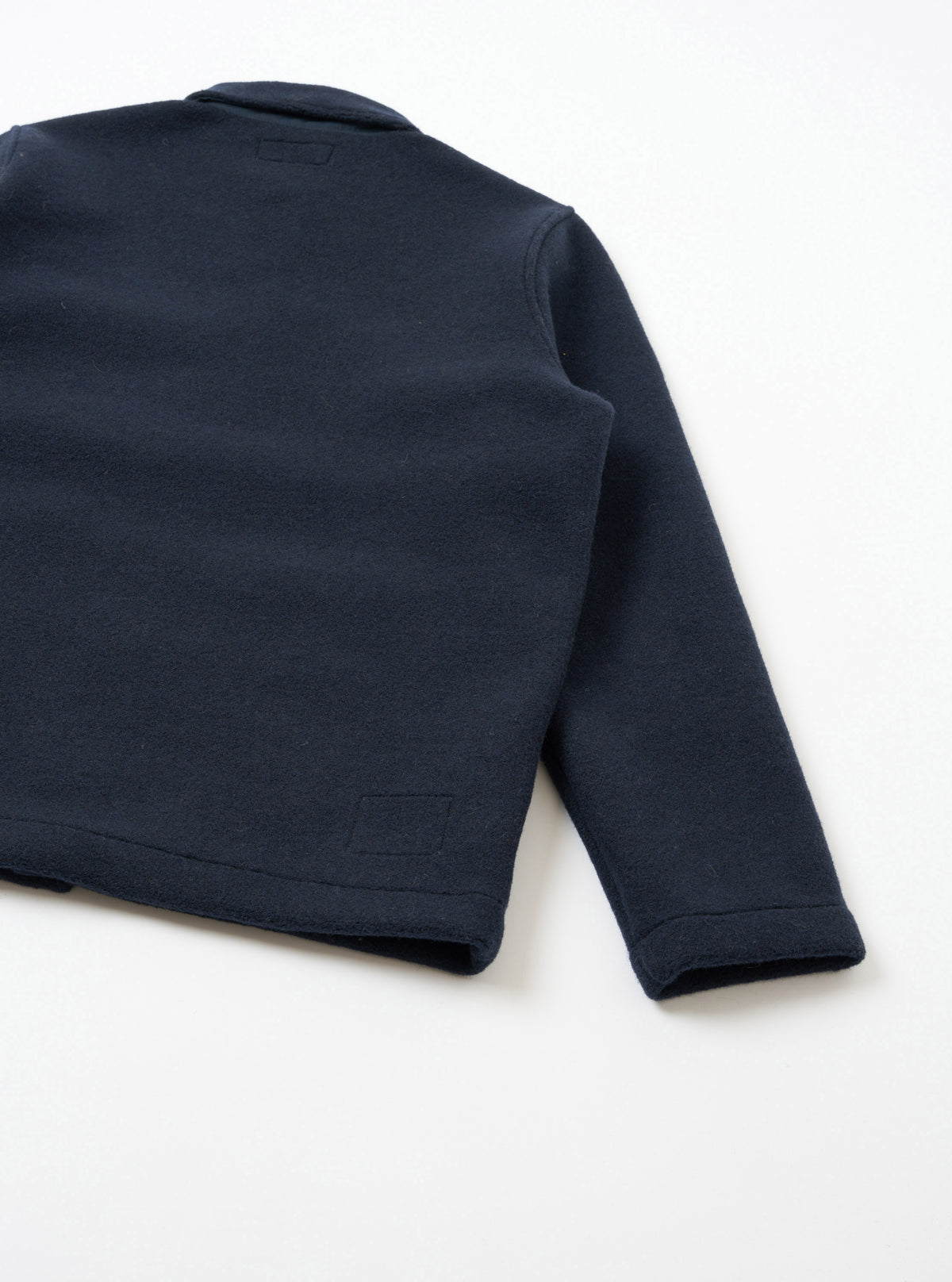 A back view photograph of the Navy Techno Melton Plain Tag Jacket positioned against a clean white background, showcasing the clean rear panel construction, straight hem, and smooth navy techno melton texture.