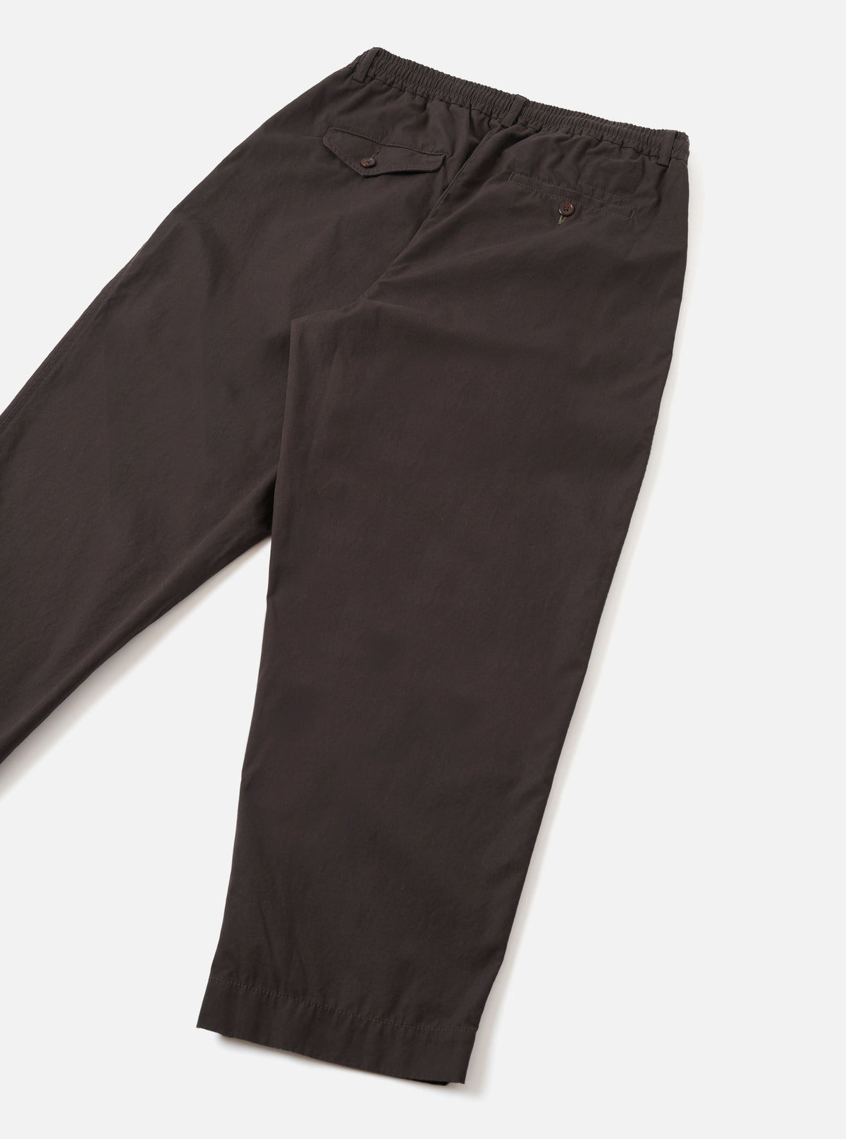 Rear view photograph of the Brown Micro Canvas Oxford Pant set against a plain white studio backdrop. The image shows the back pocket construction, clean hem finish, and loose silhouette of the brown micro-canvas cotton trousers.