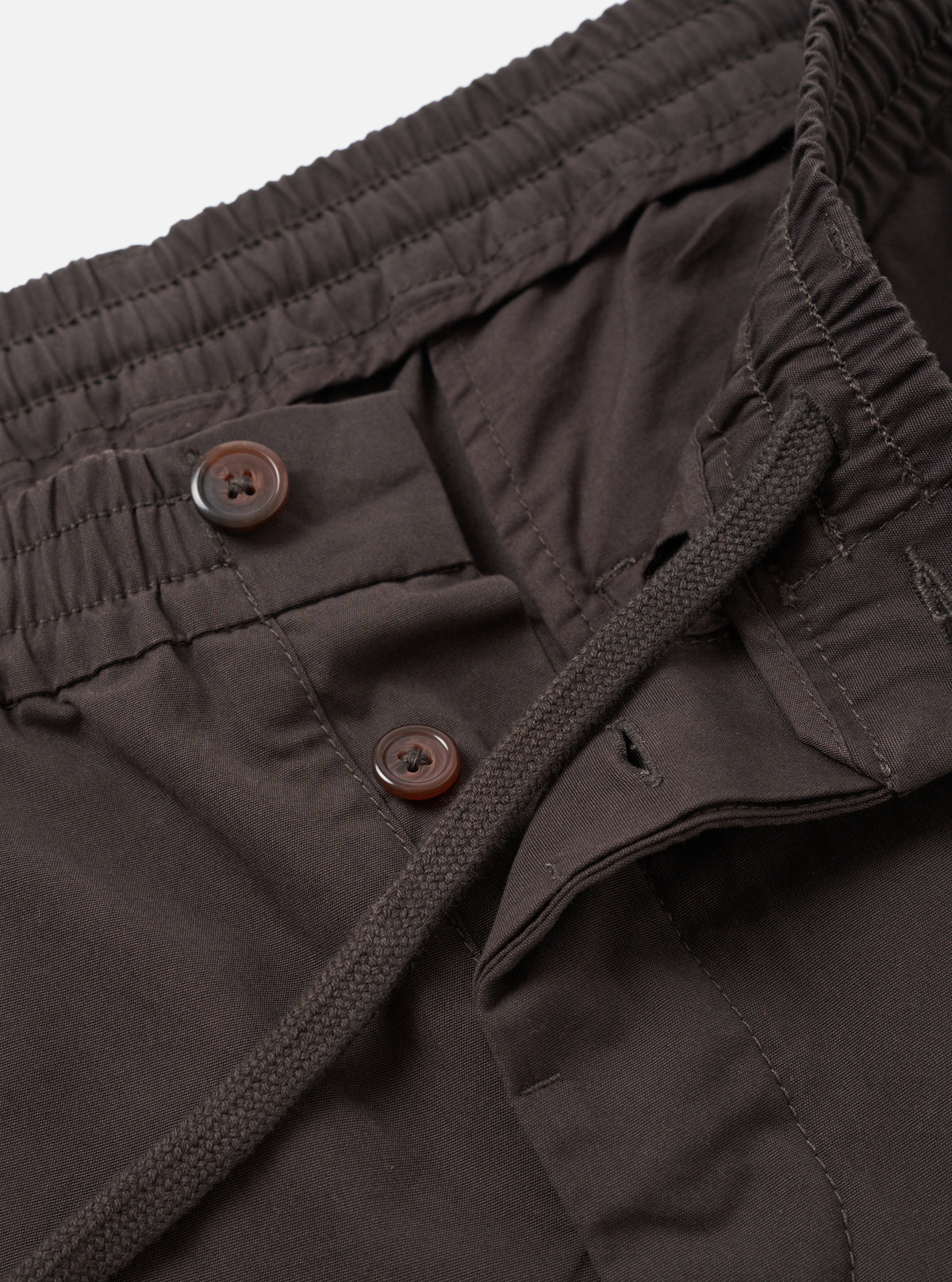 Detailed close-up view of the Brown Micro Canvas Oxford Pant on a clean studio background. The photo highlights the drawstring waistband, pleat construction, side seam pockets, and detailed brown cotton micro-canvas fabric texture.
