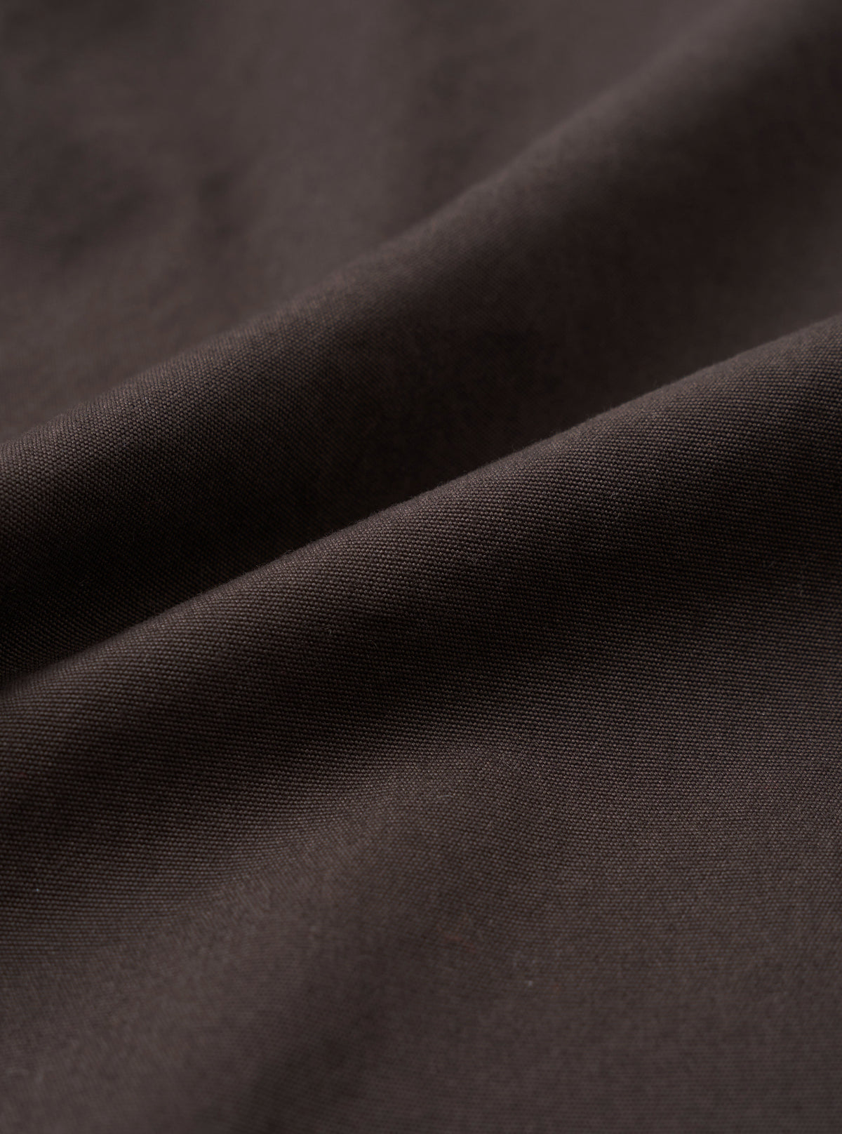 A close-up fabric swatch image of the Brown Micro Canvas Oxford Pant set against a solid white background, displaying the tight weave, fine surface texture, and natural shade of the brown cotton canvas material.