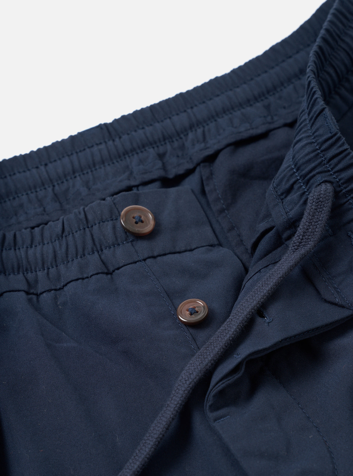 Close-up detail shot of the Navy Micro Canvas Oxford Pant set on a plain studio background. The image highlights the adjustable drawstring waist, front pleats, slash side pockets, and fine navy blue micro-canvas weave.
