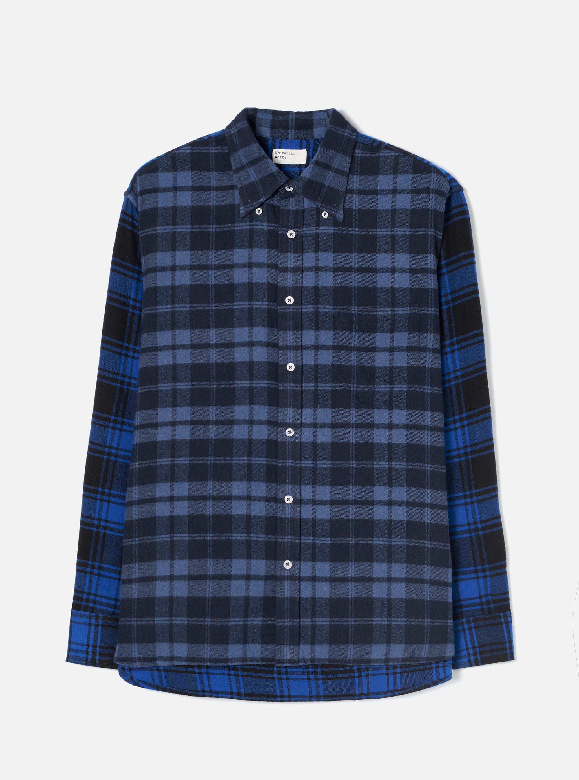 Flat lay of a Universal Works navy and blue brushed flannel check shirt on a light grey studio backdrop. The body features a navy and slate check while the sleeves and hem panel use a contrasting bright blue, black and navy tartan. Point collar with button-down tabs, white buttons down the placket, a chest patch pocket, and a curved shirttail hem.