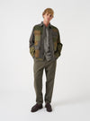 A full-length studio shot of a model wearing the Olive Patchwork Twill MW Fatigue Jacket against a neutral background. The photo showcases the military jacket styling, front button closure, flap pockets, and patchwork twill fabric.