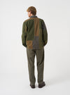 A detailed close-up shot of a model wearing the Olive Patchwork Twill MW Fatigue Jacket in a studio environment. The image highlights the textured patchwork twill cotton construction, collar details, and flap pocket design.